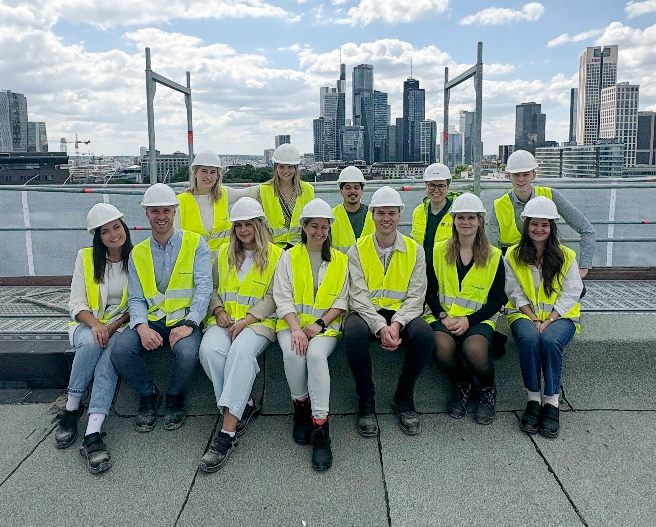 Junge BMP Projektmanager:innen auf einem Gruppenfoto beim Treffen Frankfurt mit Skyline.