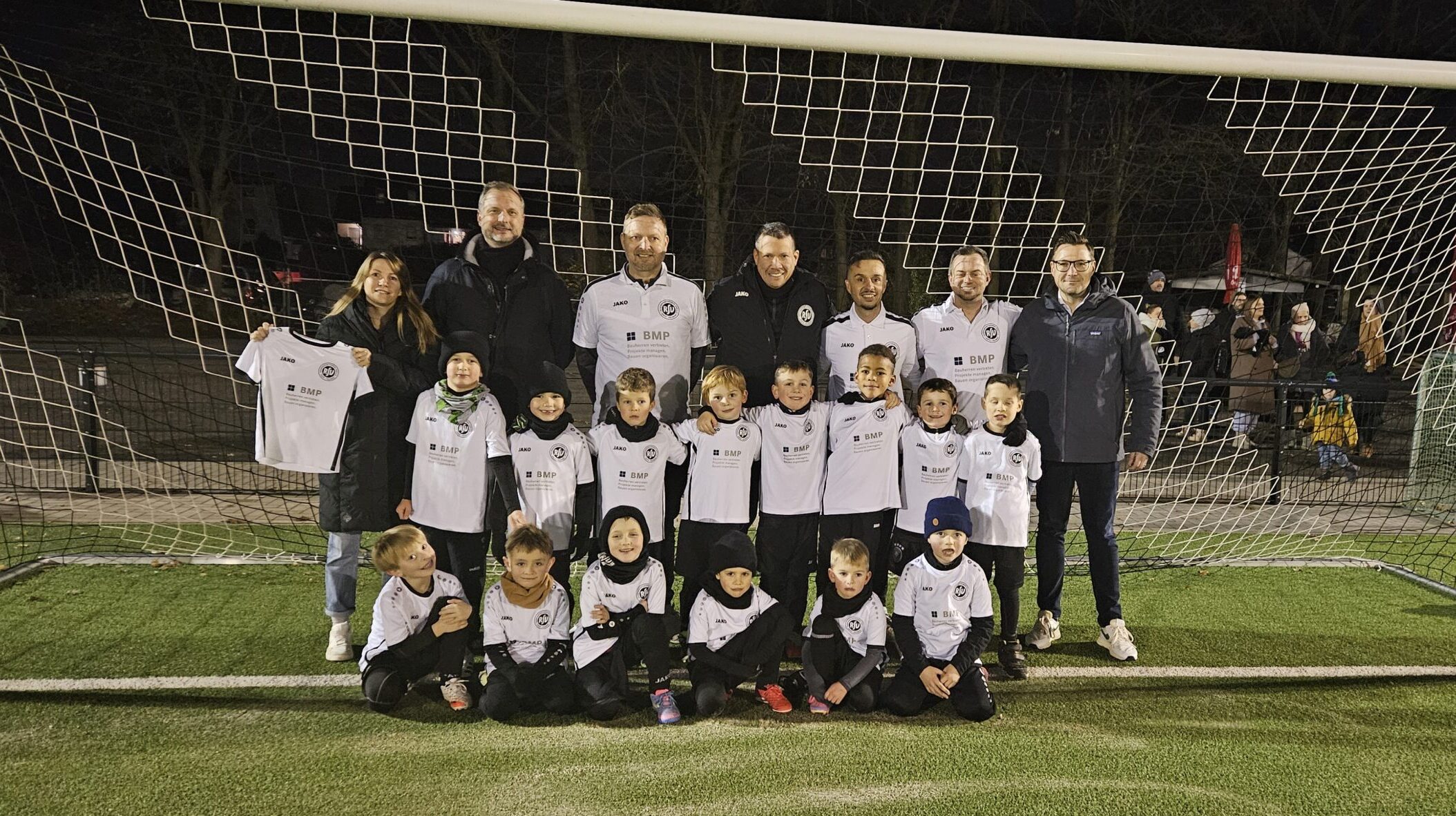 Die U7 des RSV Rath-Heumar präsentiert neue BMP Trikots auf einem Gruppenfoto auf dem Fußballplatz.