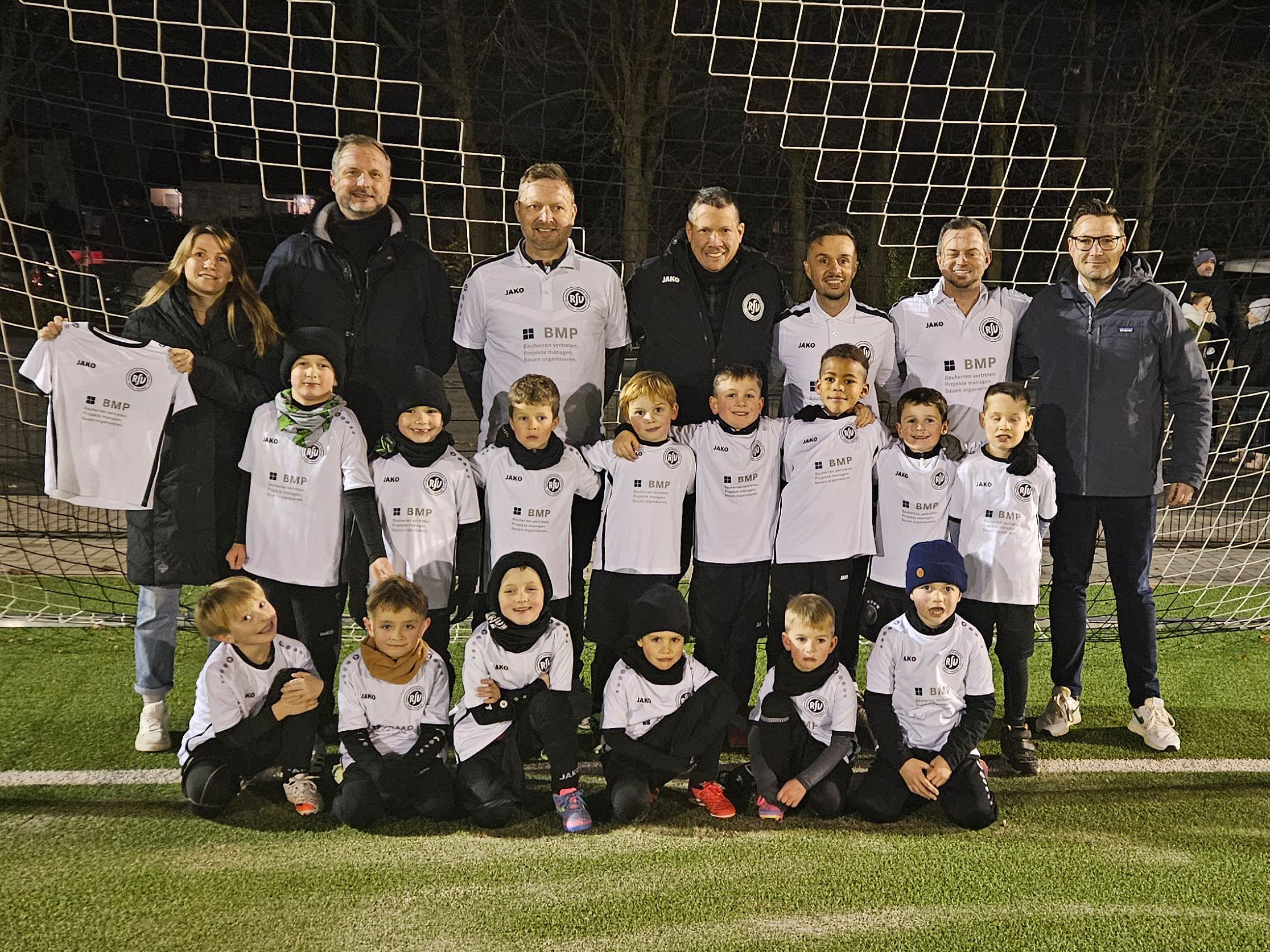 Die U7 des RSV Rath-Heumar präsentiert neue BMP Trikots auf einem Gruppenfoto auf dem Fußballplatz.