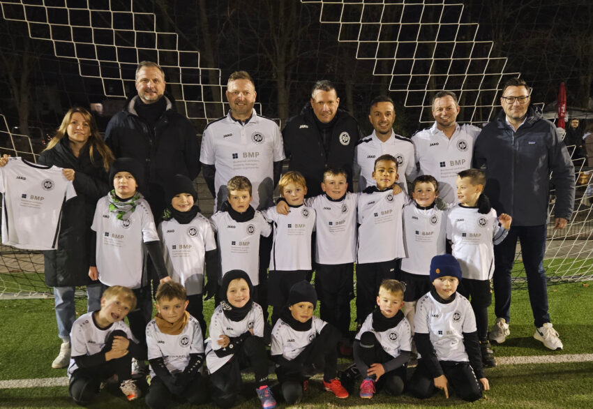 Die U7 des RSV Rath-Heumar präsentiert neue BMP Trikots auf einem Gruppenfoto auf dem Fußballplatz.