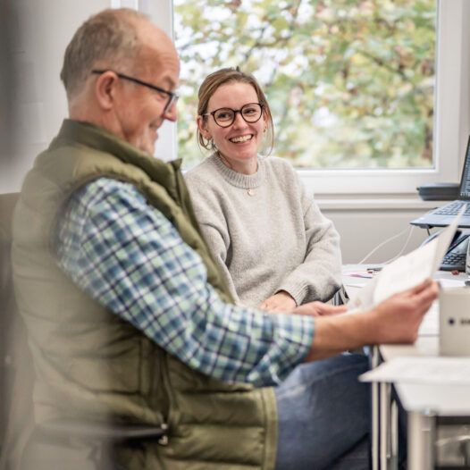 Zwei BMP-Mitarbeitende sitzen gemeinsam im Büro und besprechen Unterlagen in entspannter Atmosphäre.