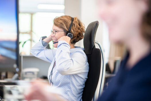 BMP-Mitarbeiterin mit Headset arbeitet lächelnd an ihrem Arbeitsplatz im Büro.