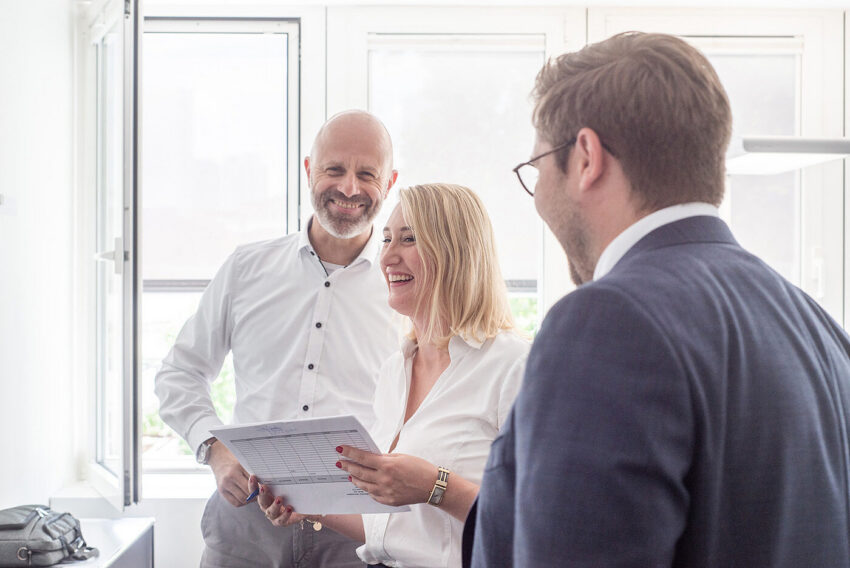Drei Mitarbeitende von BMP Projektmanagement besprechen Unterlagen in einem hellen Büroraum.