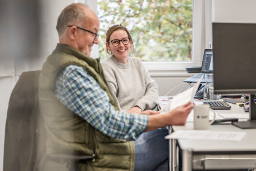 Zwei Mitarbeitende von BMP besprechen gut gelaunt Unterlagen in einem hellen Büro.