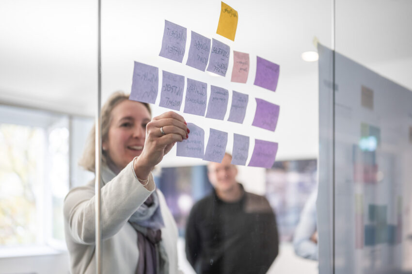 BMP-Team organisiert Workshop-Ideen mit Post-its an einer Glaswand im Konferenzraum.