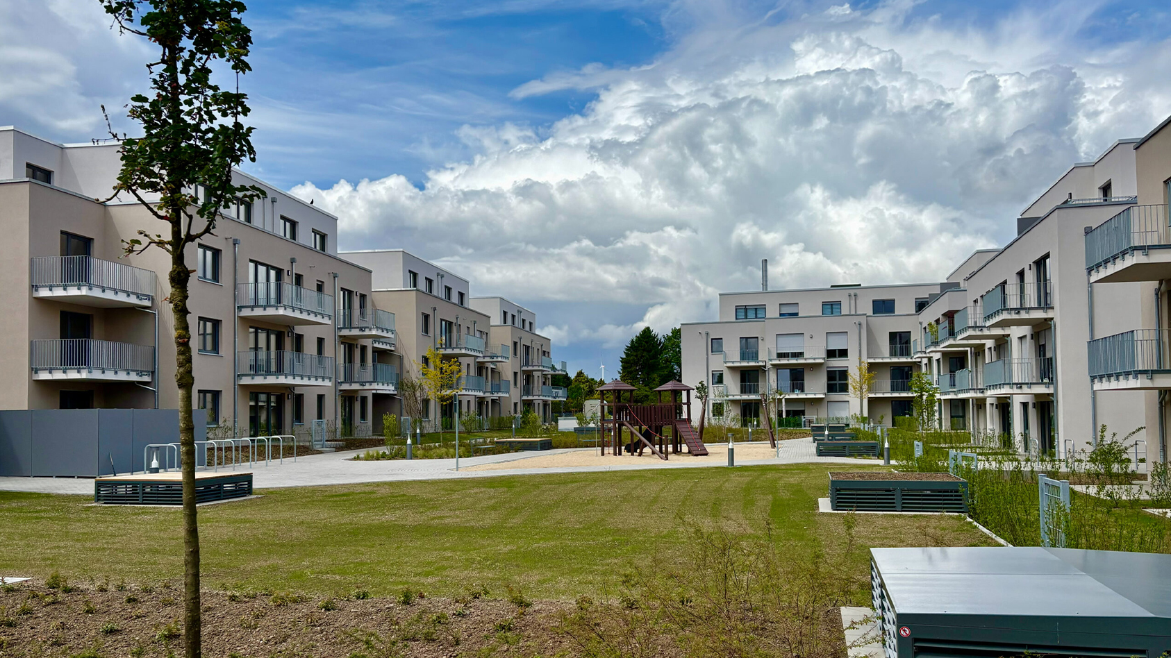 Moderne Wohnanlage mit begrüntem Innenhof, Spielplatz und Sitzbänken unter blauem Himmel.