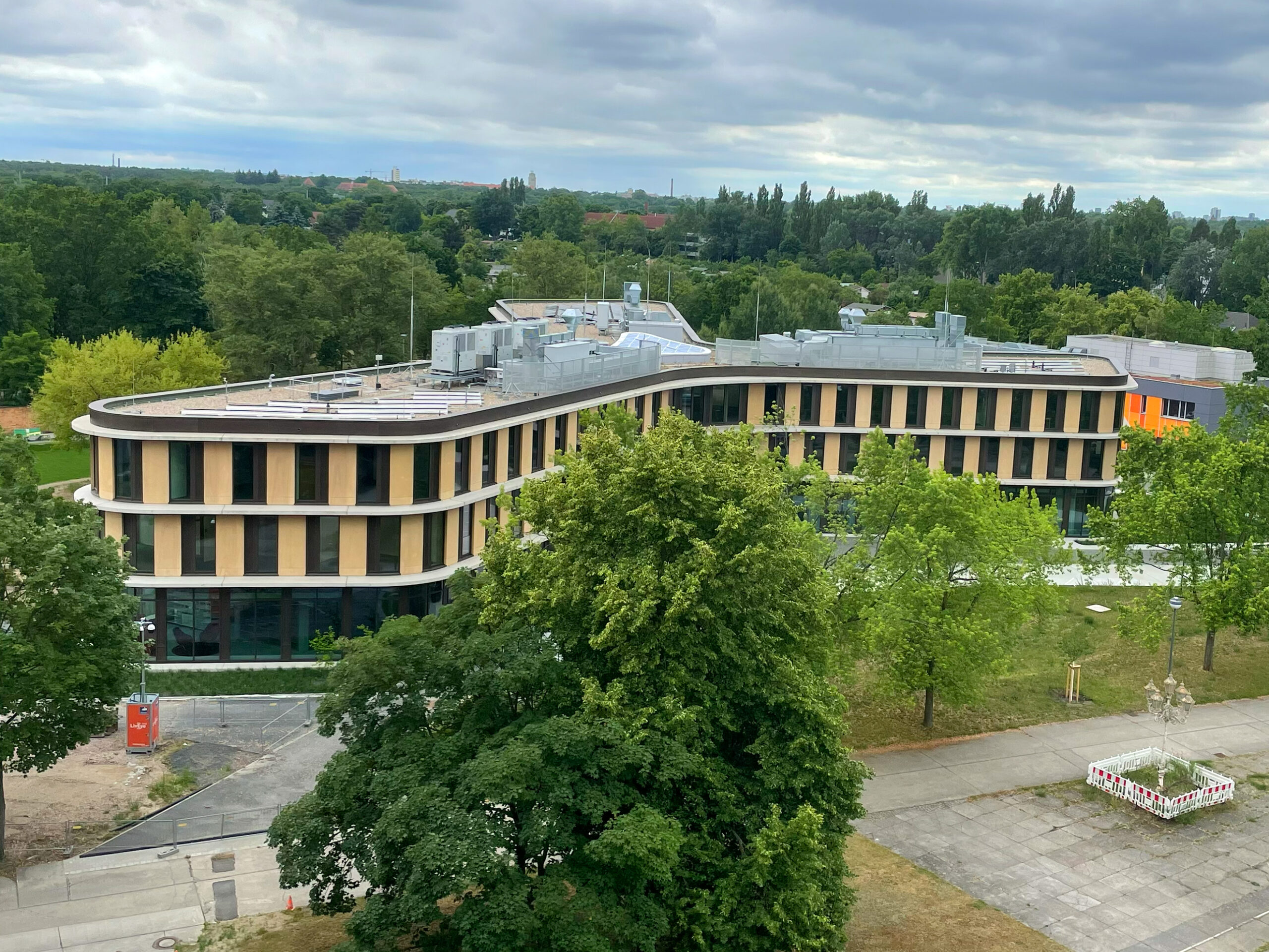 Erhöhte Außenansicht des Lise-Meitner-Hauses in Berlin-Karlshorst mit geschwungener Holzfassade und begrüntem Umfeld.