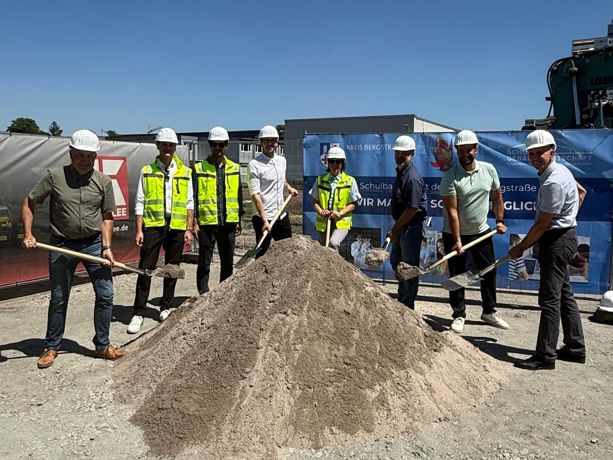 Projektbeteiligte vor einem Sandberg mit einer Schaufel in der Hand beim Spatenstich für das Lessing-Gymnasium.