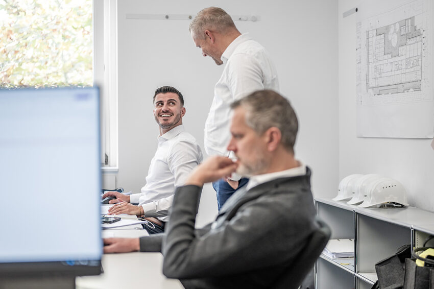 Drei BMP Mitarbeiter besprechen gemeinsam ein Bauprojekt anhand von Planungsunterlagen im Büro.